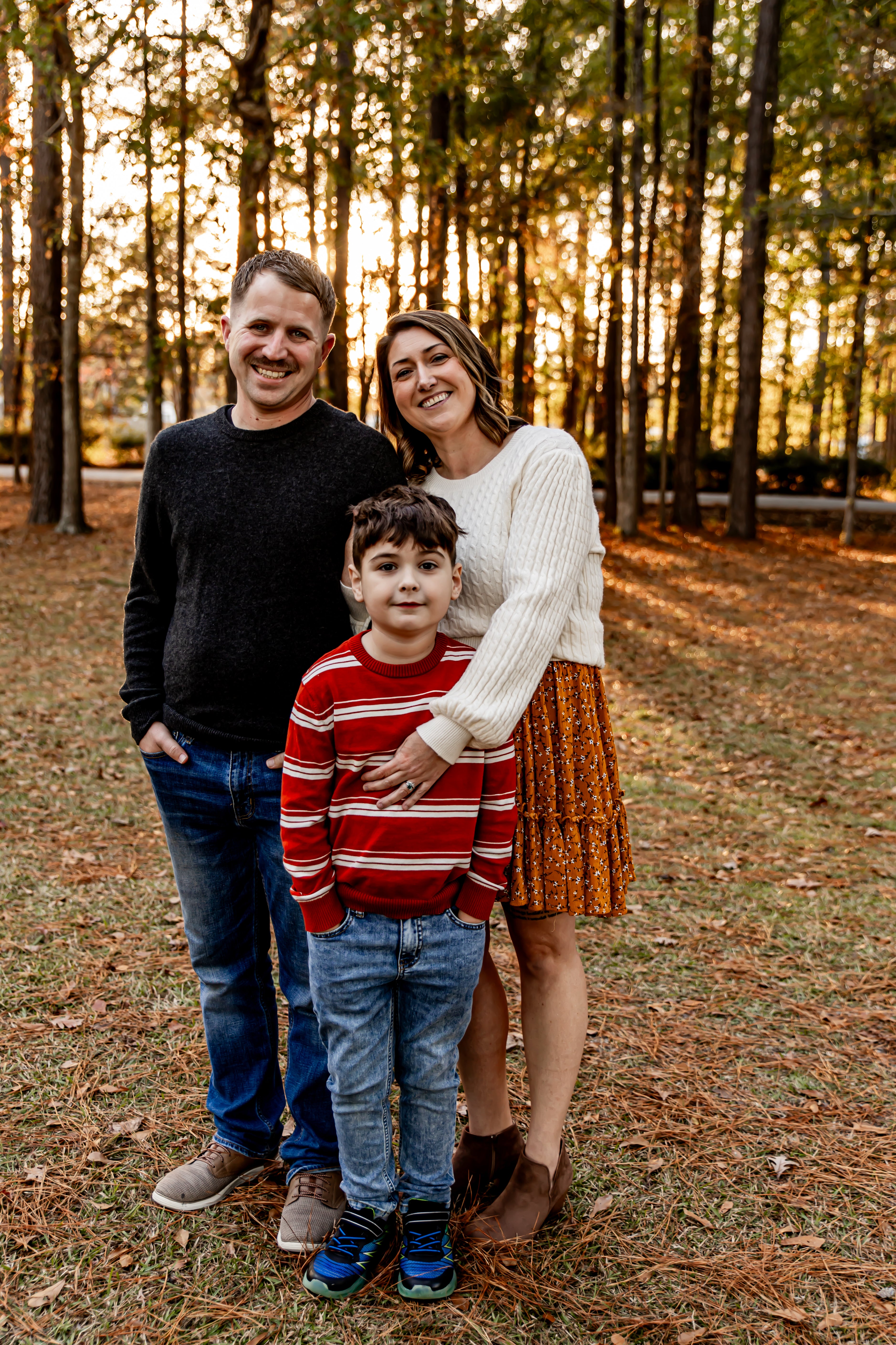 Family of three standing in a forest during sunset