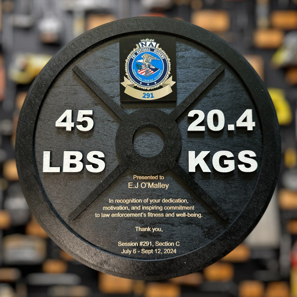 Weight plate with 45 lbs and 20.4 kgs markings, featuring a logo and text on a blurred background of gym equipment.