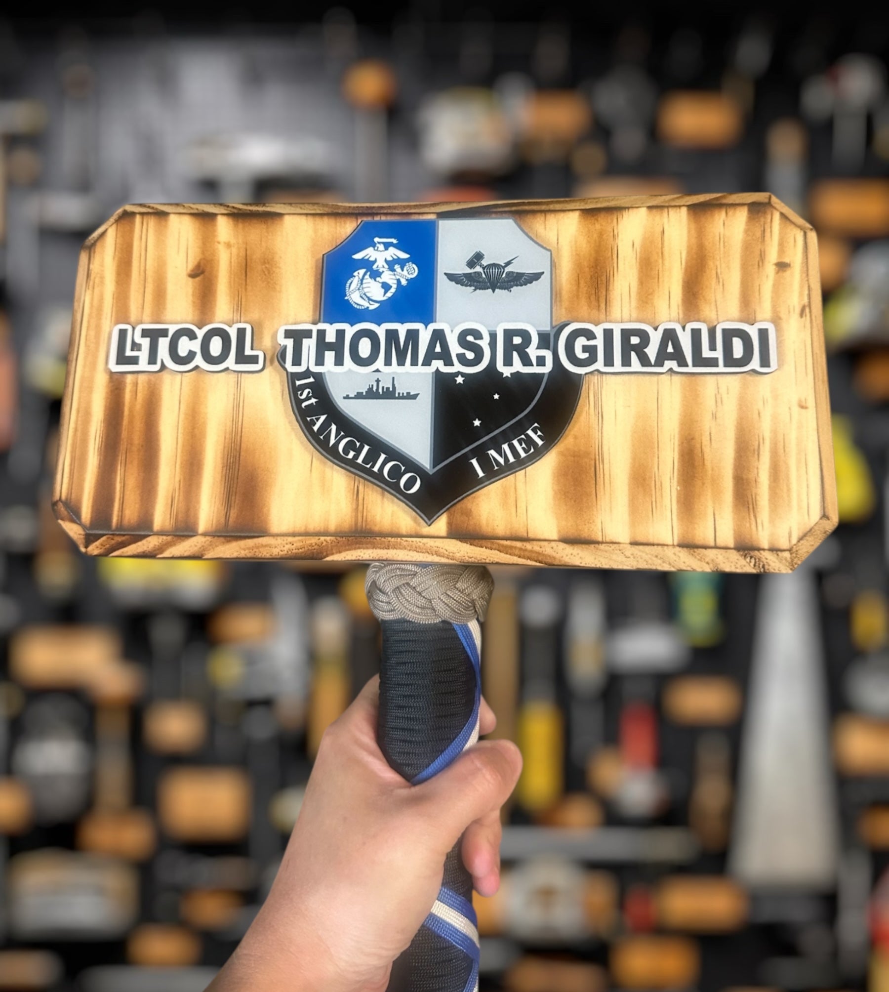 Wooden thor hammer military gift with a badge and text held by a hand against a blurred background