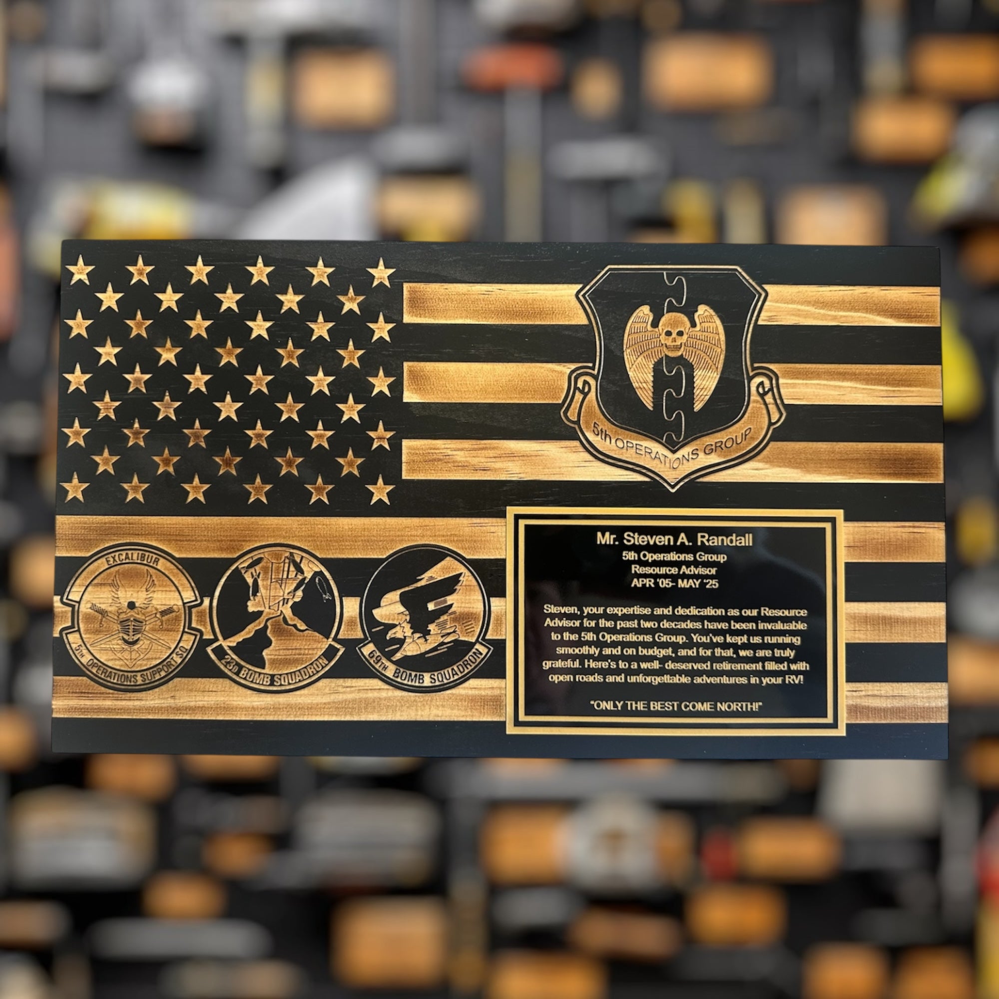 Wooden plaque with American flag design and engraved text on a blurred background