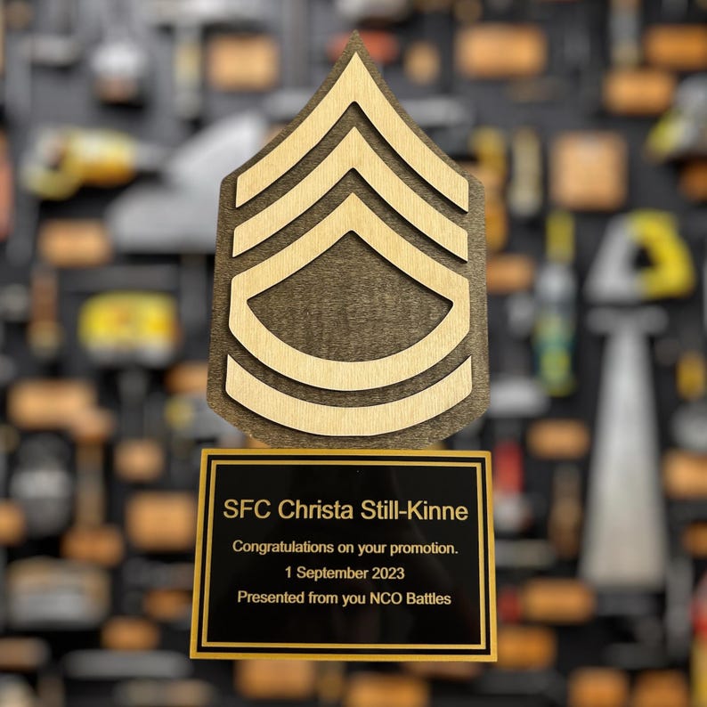 Promotion plaque with military rank insignia and personalized message on a blurred background of similar items.