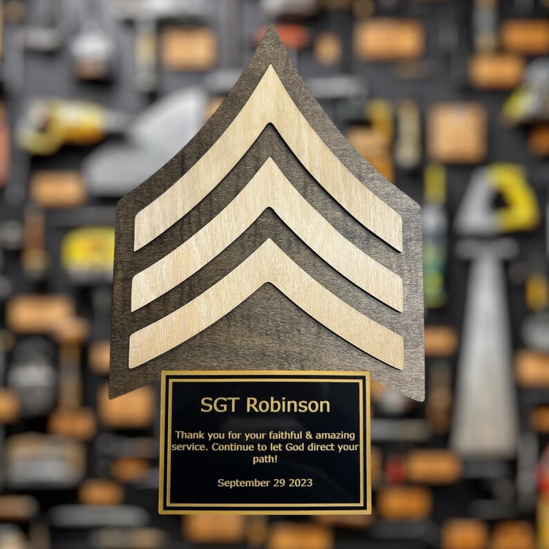 Wooden military rank insignia with engraved name and message on a blurred background of similar insignias.