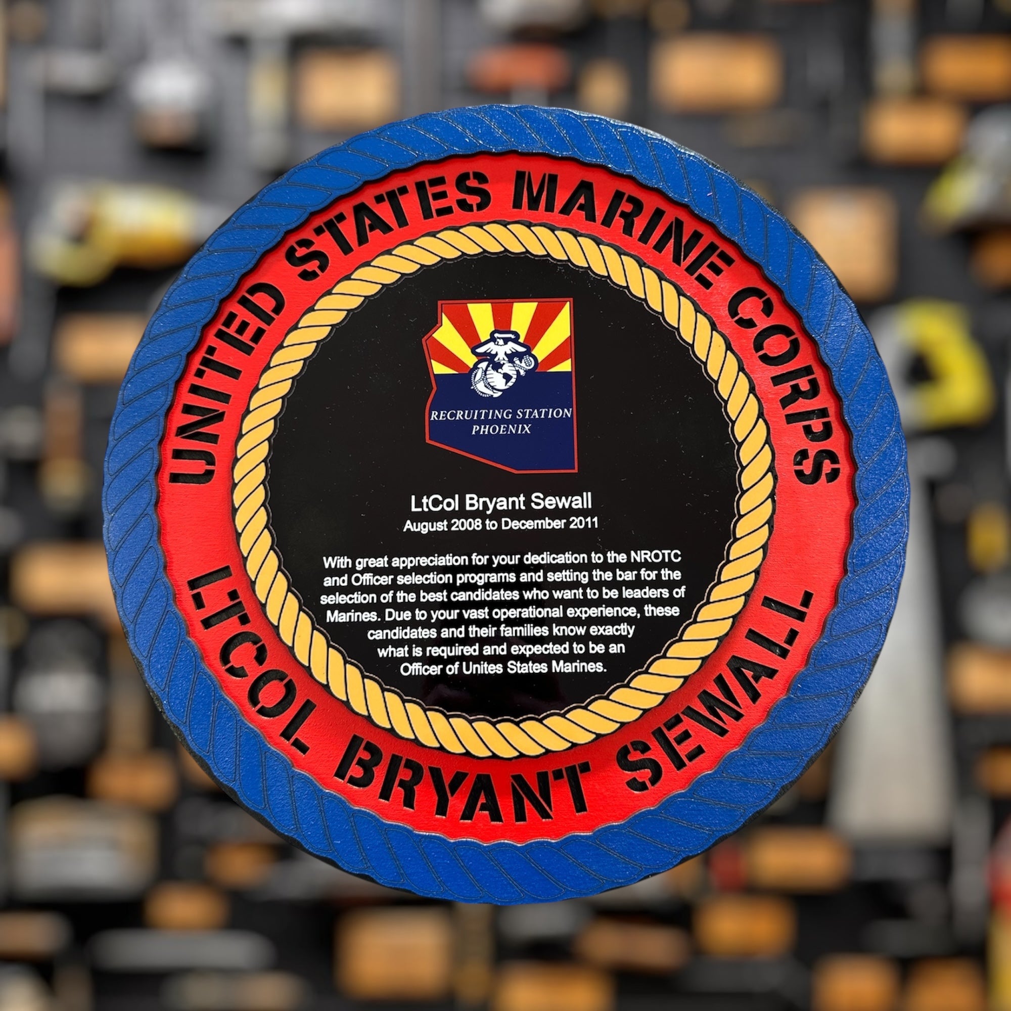 United States Marine Corps recruiting plaque with a red and blue border, featuring the name and rank 'LTCOL'  on a blurred background.